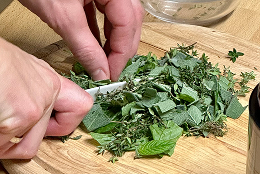 Hände schneiden frische grüne Kräuter mit einem Messer auf einem Holzbrett.