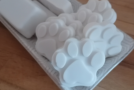 Mehrere weiße Seifenstücke in Form von Pfoten liegen auf einem Tablett aus Holz.